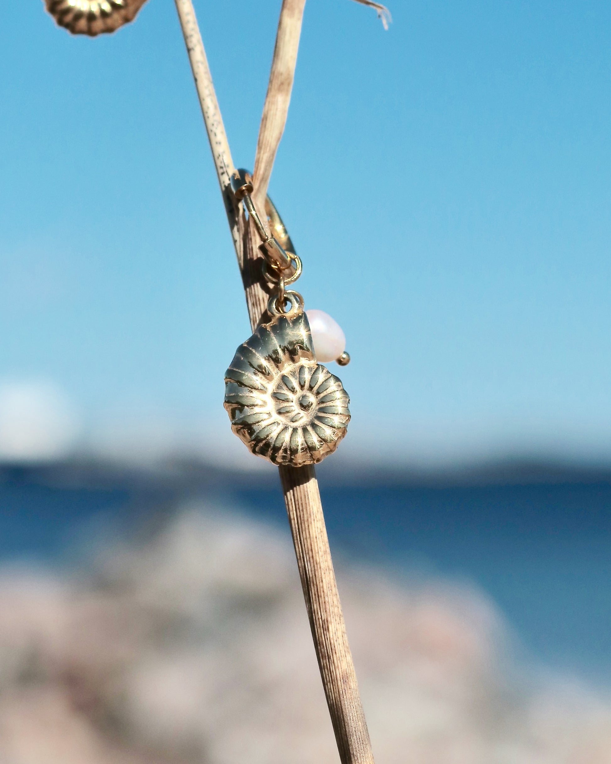 Gold-tone hoop earring with a shell charm and freshwater pearl photographed by the sea in Hanko, Finland