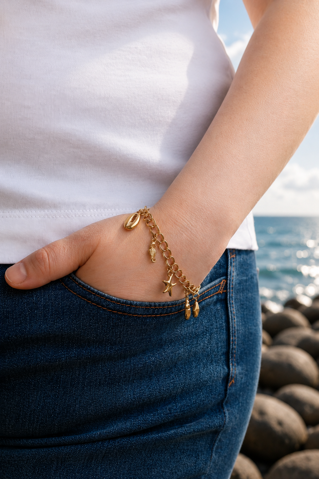 Person wearing a gold bracelet with star charms by the ocean.