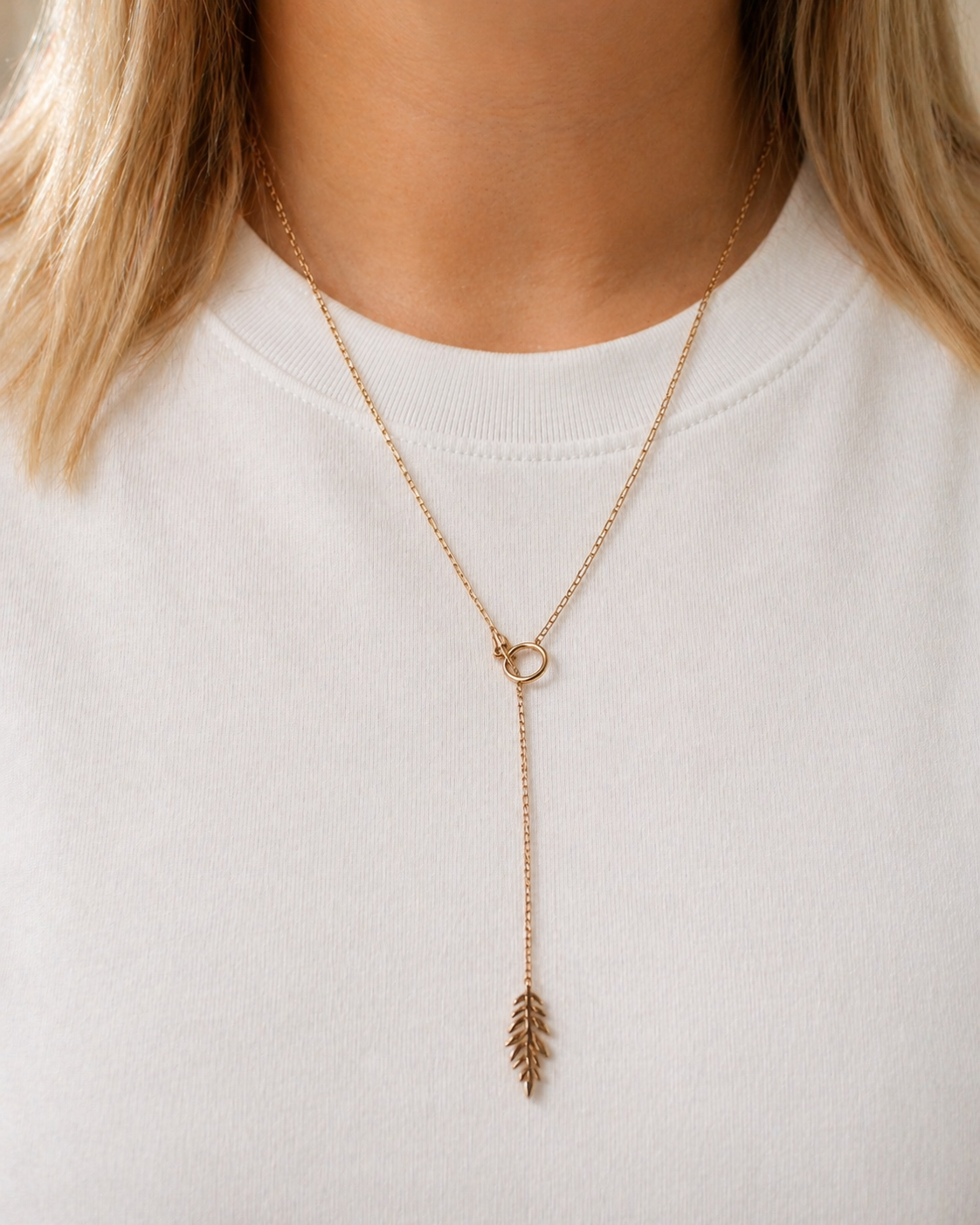 Gold necklace with a leaf pendant worn by a person on a white background