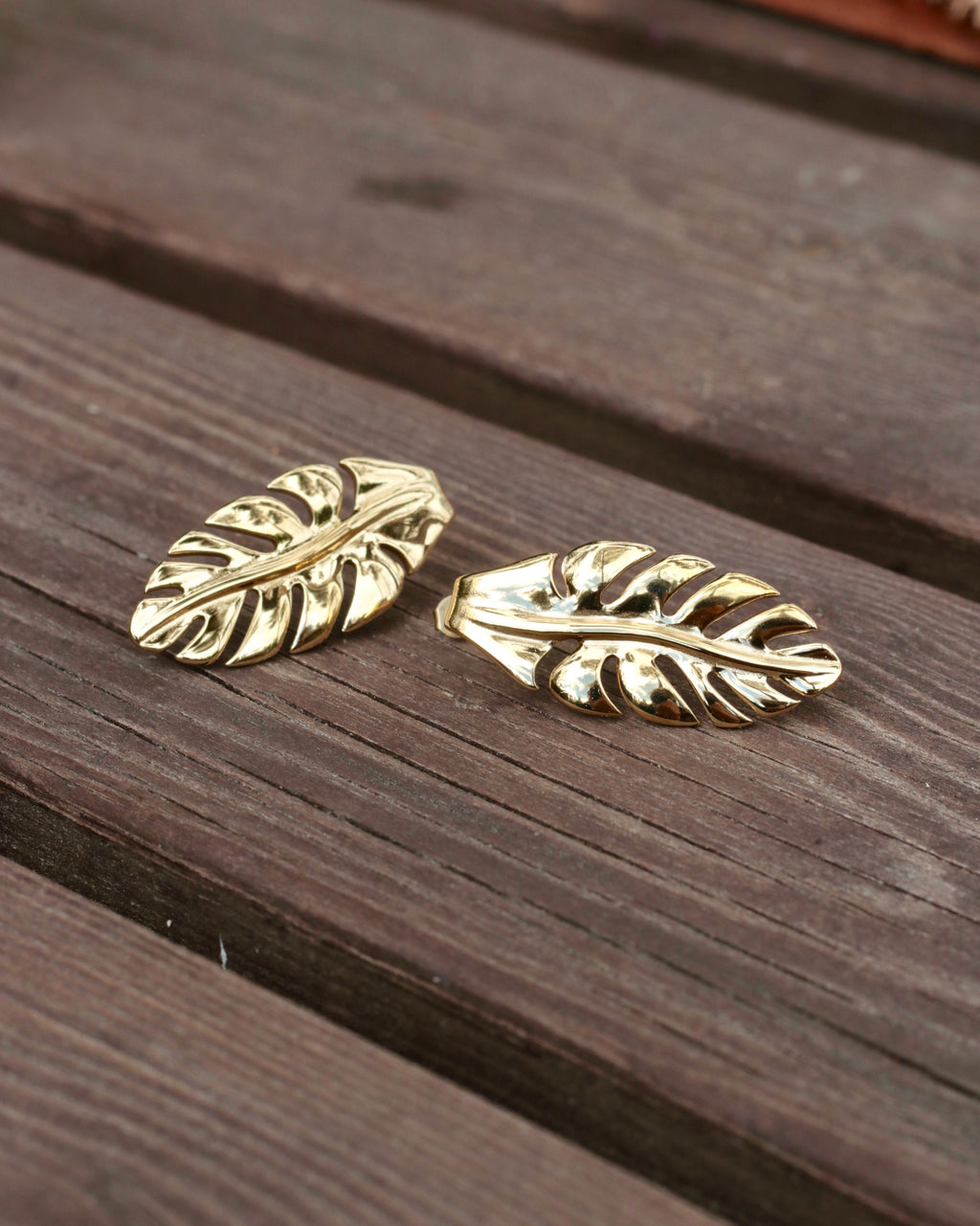 A pair of gold-toned leaf-shaped earrings resting on a dark brown wooden surface.