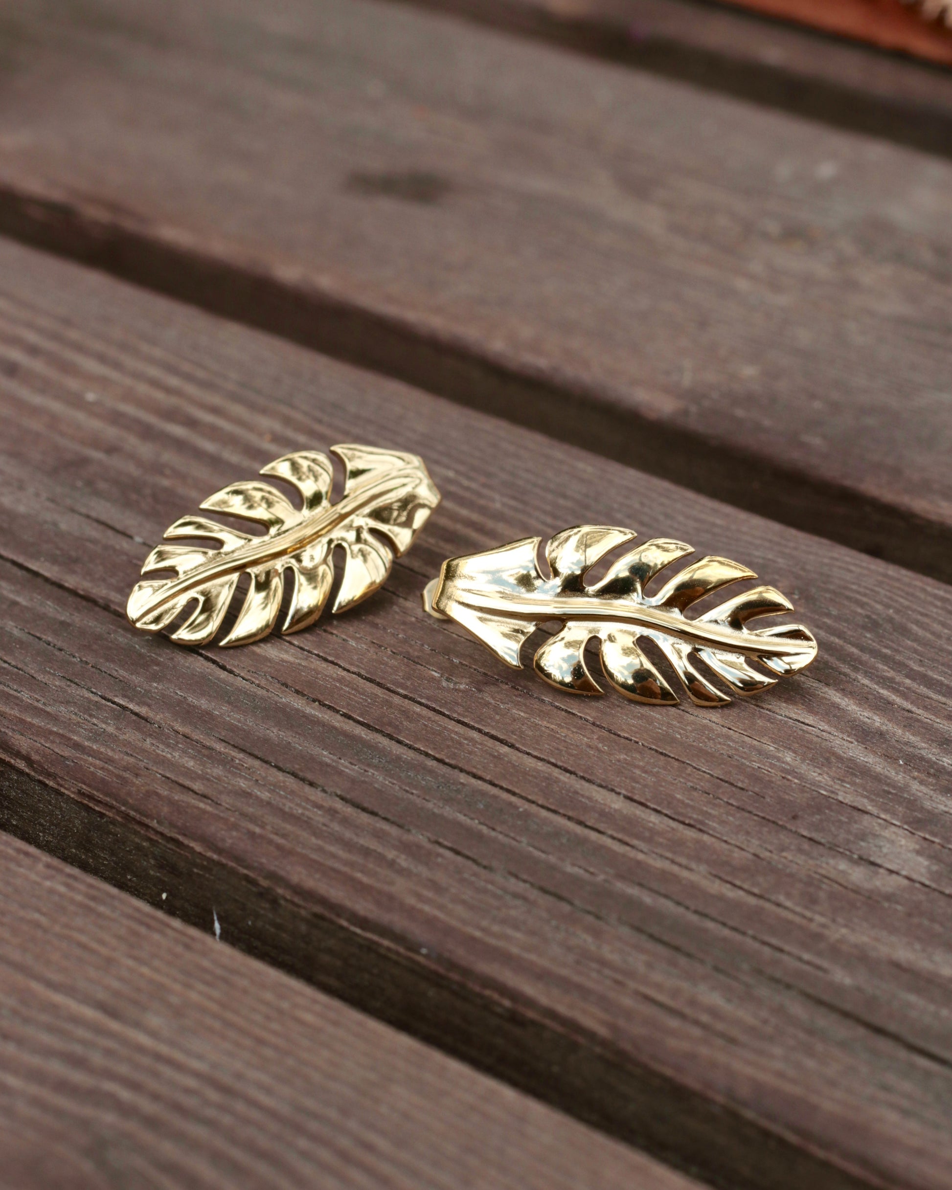 A pair of gold-toned leaf-shaped earrings resting on a dark brown wooden surface.