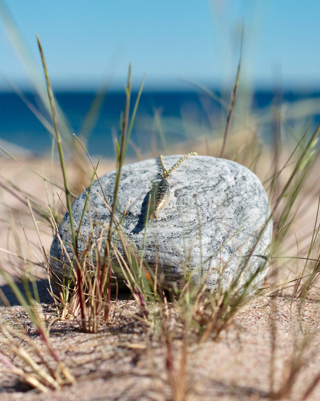 Gold-tone fish pendant necklace displayed on coastal stones at the beach in Hanko, Finland