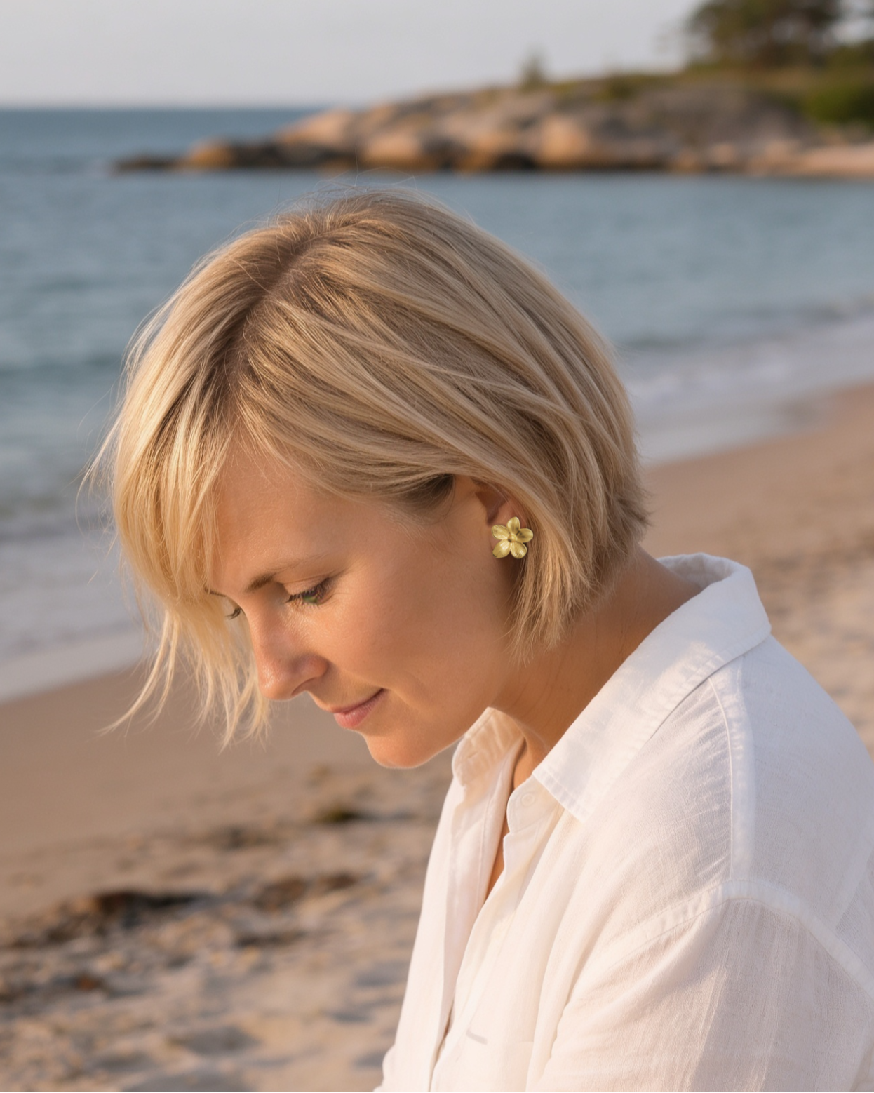 Gold flower stud earrings worn by a woman on Tulliniemi beach in Hanko, Finland.
