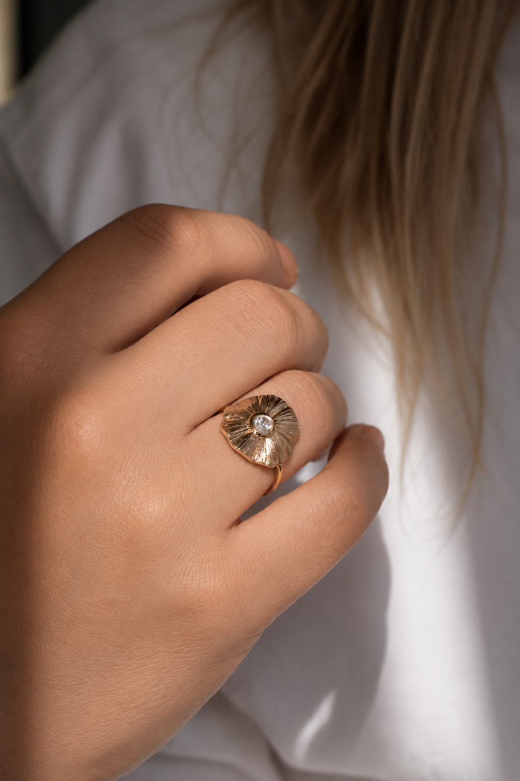 18K gold-plated floral ring with sculpted petals and a luminous center stone worn by a model by HNKO