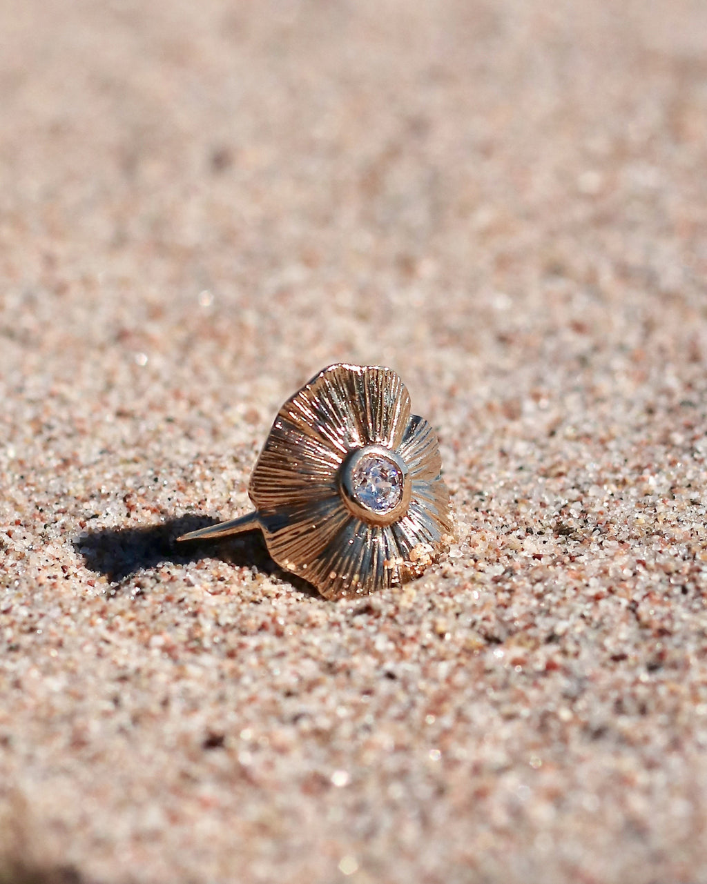 18K gold-plated floral ring with sculpted petals and a luminous center stone displayed on the beach in Hanko, Finland