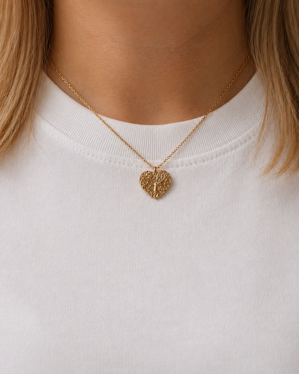 Model wearing 18K gold plated Heart Tree necklace by HNKO Finland, showing delicate openwork heart-shaped tree pendant resting naturally on neckline in minimalist lifestyle setting