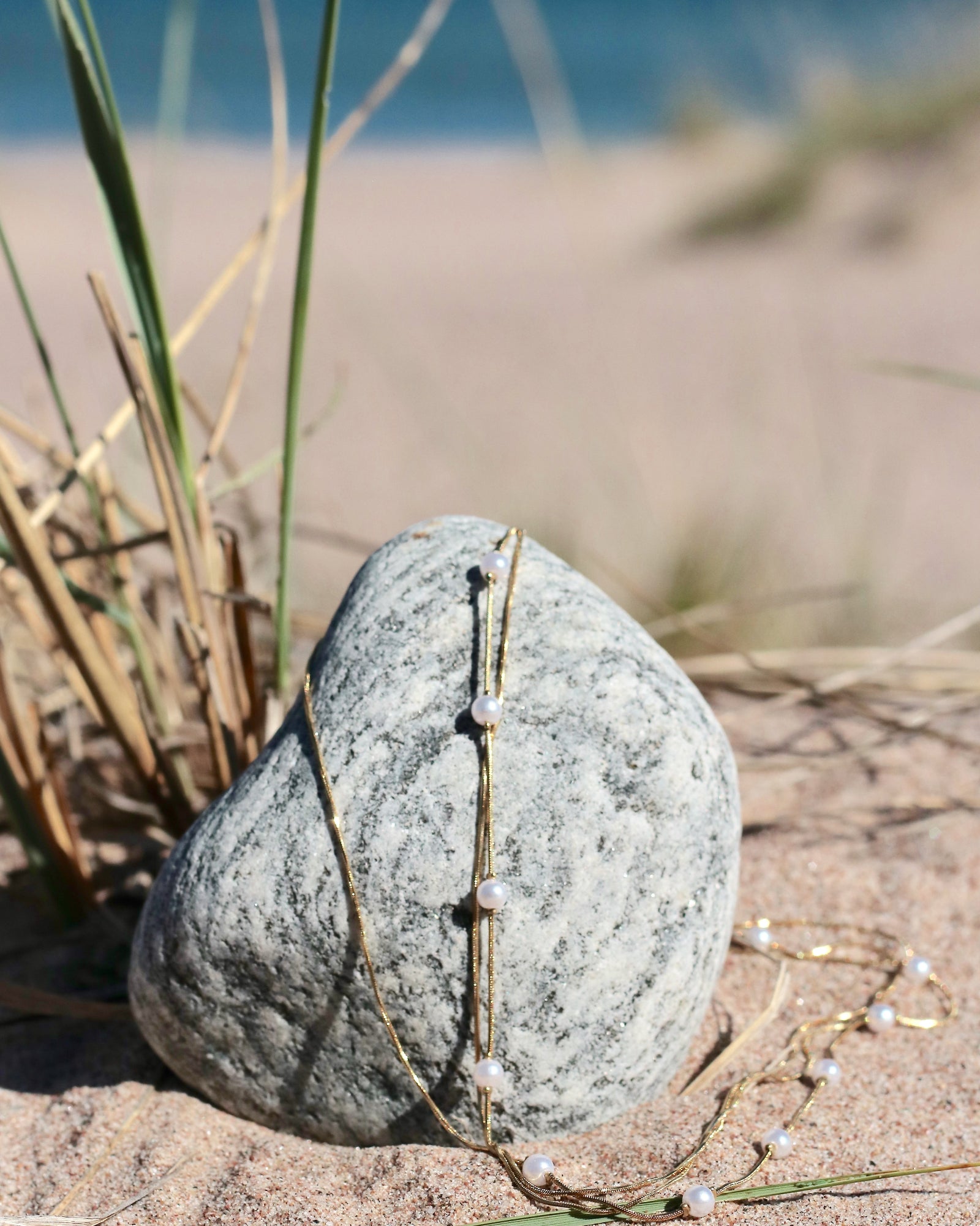 Gold-tone pearl chain necklace with delicate imitation pearls displayed on coastal stones at the beach in Hanko, Finland