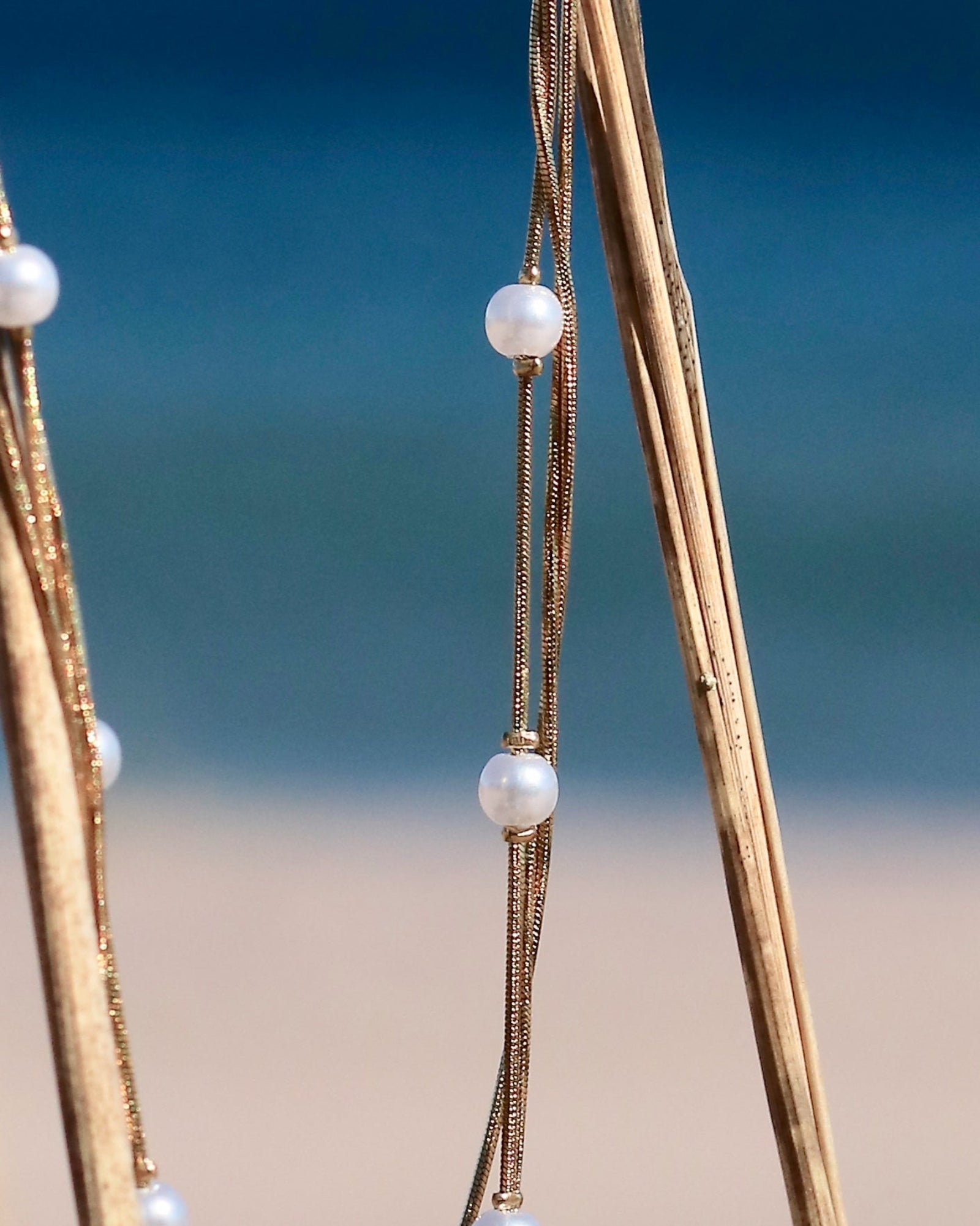 Gold-tone pearl chain necklace with delicate imitation pearls displayed on coastal vegetation in Hanko, Finland