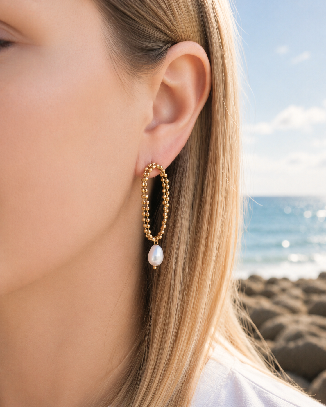 Model wearing gold-tone steel earrings with cultured pearl drops by HNKO