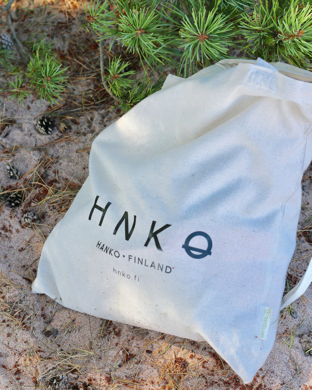 Person holding a beige tote bag with HNKQ branding outdoors