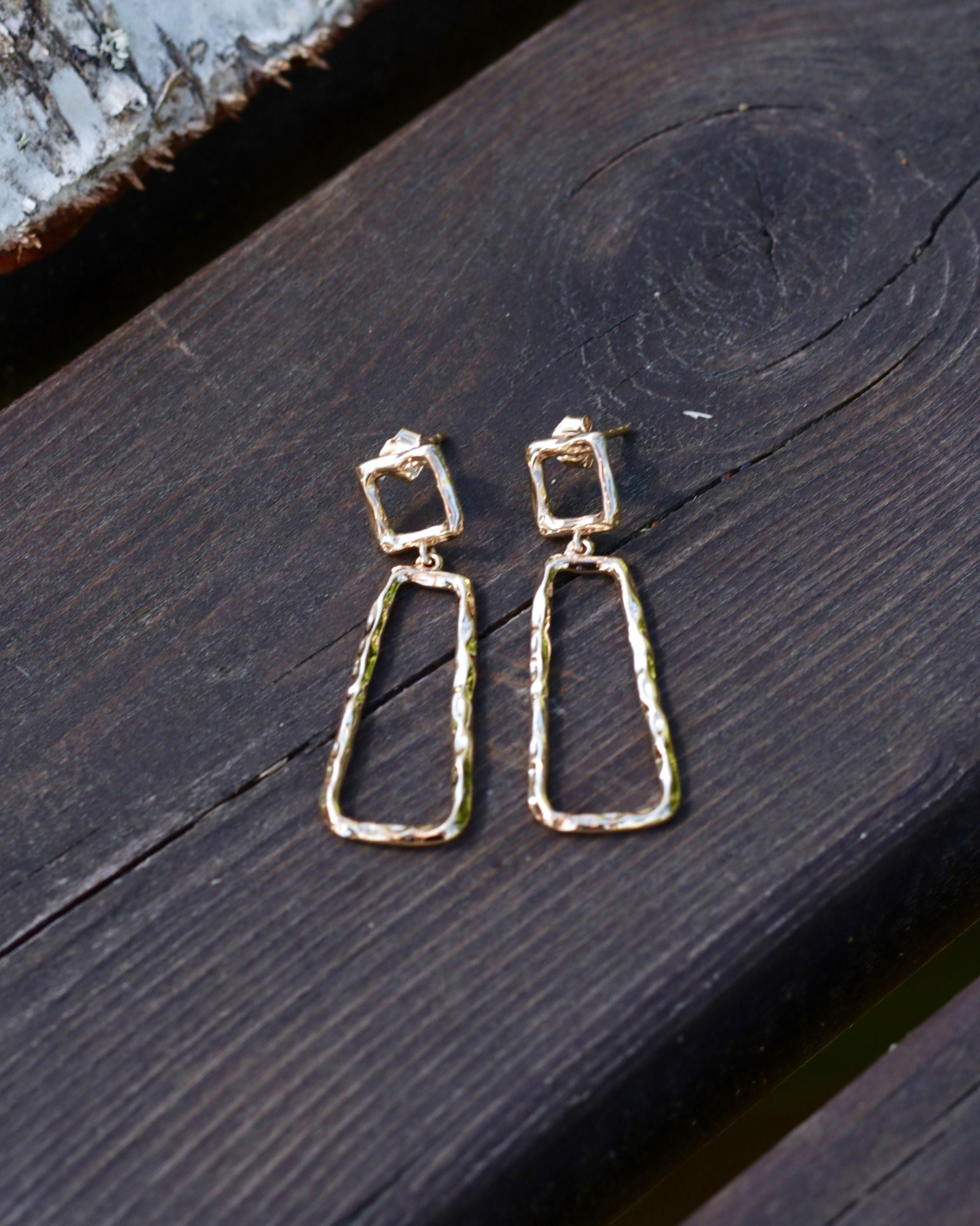 A pair of gold-toned geometric dangle earrings with textured triangular drop shapes, displayed on a dark wooden surface.