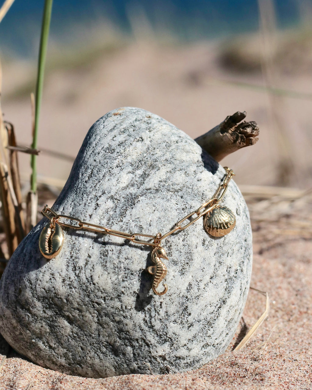 Gold tone sea charm necklace from HNKO Meri collection placed on coastal rock and beach stones, showing marine-inspired pendants inspired by Nordic shoreline and natural seaside textures in Hanko Finland