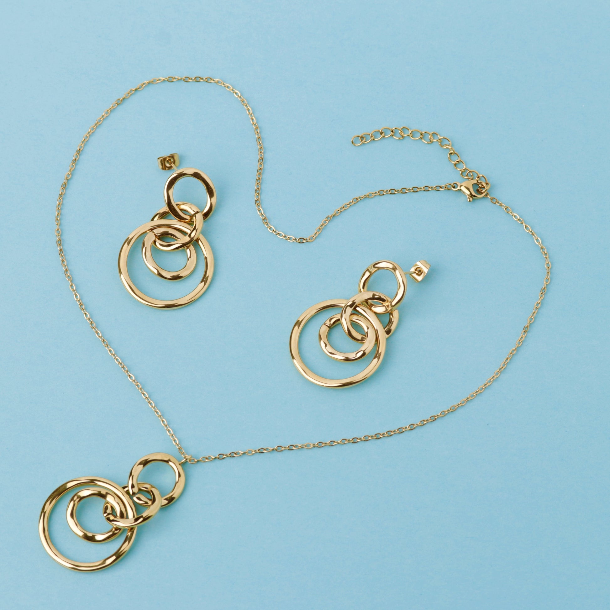 Gold jewelry set featuring a necklace and matching earrings with interlocking circular ring pendants, displayed on a light blue background.